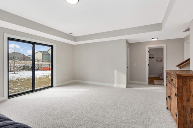 empty room with baseboards, stairway, a raised ceiling, and light colored carpet