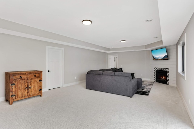 carpeted living area with a warm lit fireplace, baseboards, and a raised ceiling