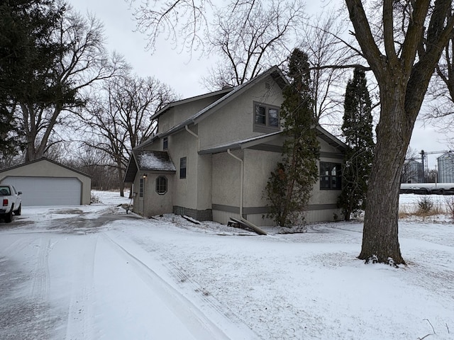 view of snow covered exterior featuring an outdoor structure, a detached garage, and stucco siding