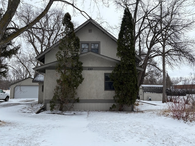 view of snow covered exterior featuring a garage, stucco siding, and an outdoor structure