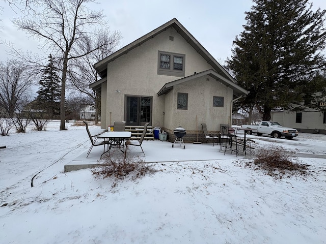 snow covered rear of property featuring stucco siding