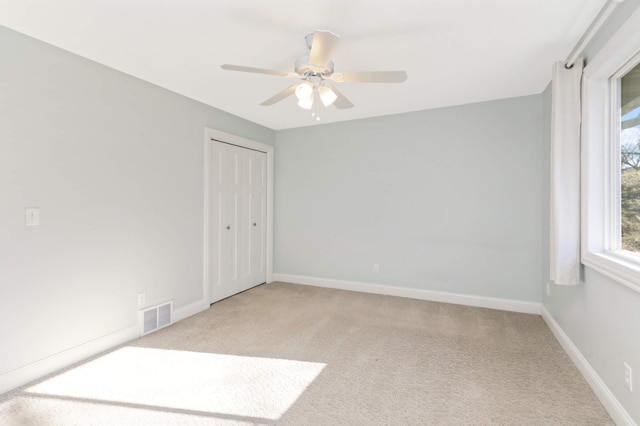 spare room with visible vents, a ceiling fan, baseboards, and light carpet