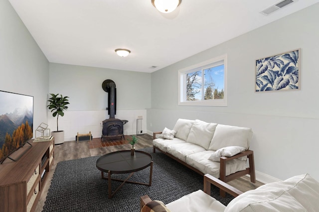living area featuring a wood stove, radiator heating unit, baseboards, wood finished floors, and visible vents