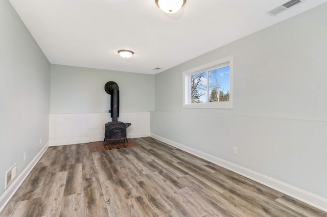 unfurnished living room with baseboards, a wood stove, wood finished floors, and visible vents