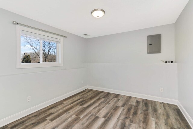 empty room with baseboards, wood finished floors, and electric panel