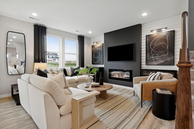 living area with a glass covered fireplace, visible vents, light wood finished floors, and recessed lighting