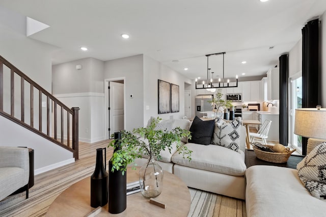 living room featuring stairs, light wood-type flooring, a notable chandelier, and recessed lighting