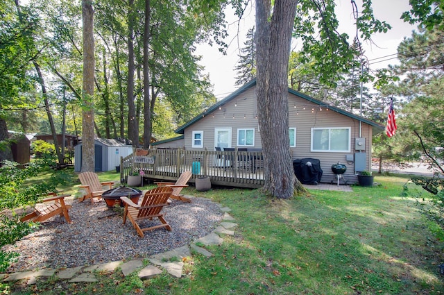 rear view of property with a fire pit, a shed, a wooden deck, a yard, and an outdoor structure