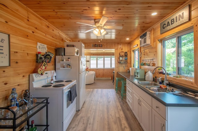 kitchen with dark countertops, wooden walls, a healthy amount of sunlight, white appliances, and a sink