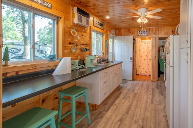 kitchen featuring a sink, wood ceiling, wood walls, and white cabinetry