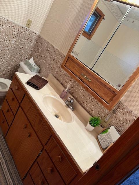 bathroom with backsplash, vanity, toilet, and tile walls