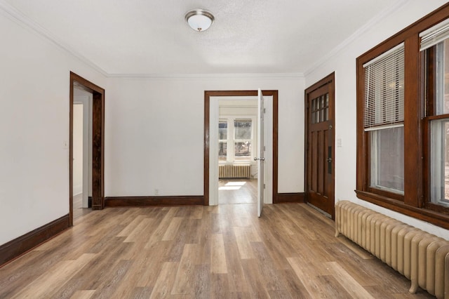 empty room with radiator, light wood finished floors, and ornamental molding