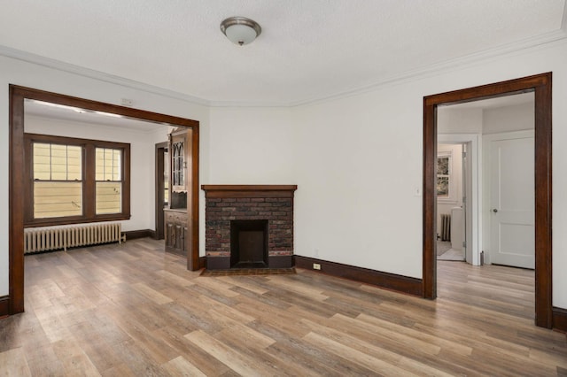 unfurnished living room featuring a brick fireplace, baseboards, radiator heating unit, ornamental molding, and wood finished floors