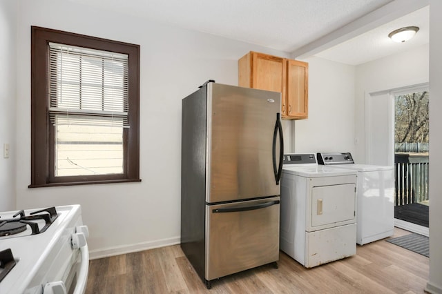 kitchen with washing machine and clothes dryer, a wealth of natural light, freestanding refrigerator, and light wood-style floors