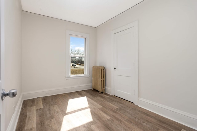 empty room with radiator, wood finished floors, and baseboards