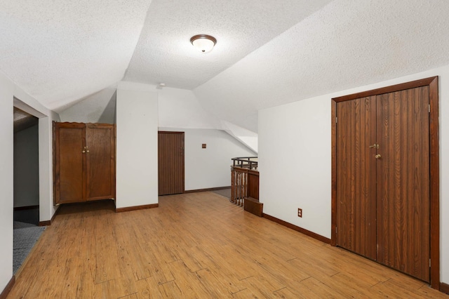 bonus room featuring baseboards, a textured ceiling, lofted ceiling, and light wood-style floors