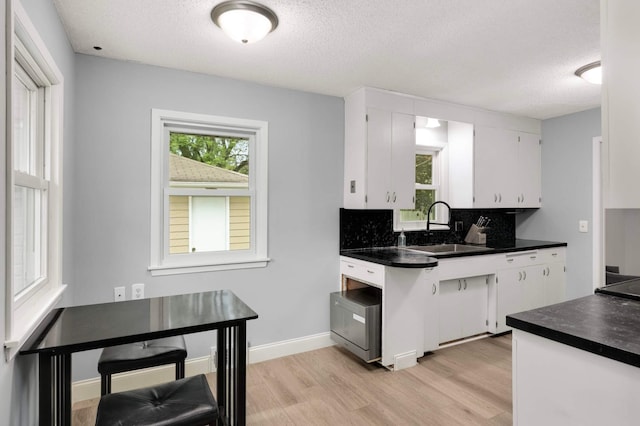 6719 Ewing Ave N, Brooklyn Center, MN 55429 - kitchen with a sink, backsplash, white cabinetry, light wood-type flooring, and a textured ceiling