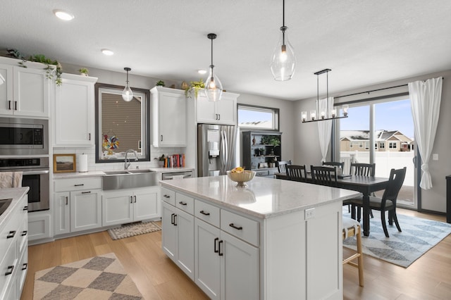 kitchen with a center island, light wood-style flooring, white cabinets, stainless steel appliances, and a sink