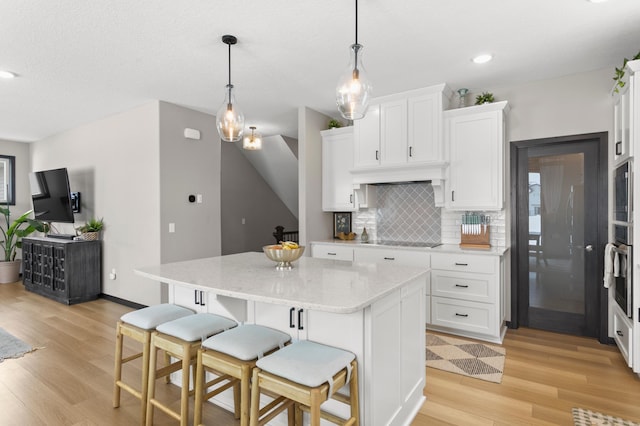 kitchen featuring backsplash, a center island, black electric stovetop, stainless steel oven, and white cabinets