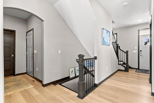 foyer entrance featuring arched walkways, light wood finished floors, and baseboards