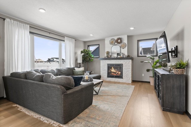 living room with a wealth of natural light, a stone fireplace, light wood-style flooring, and a textured ceiling