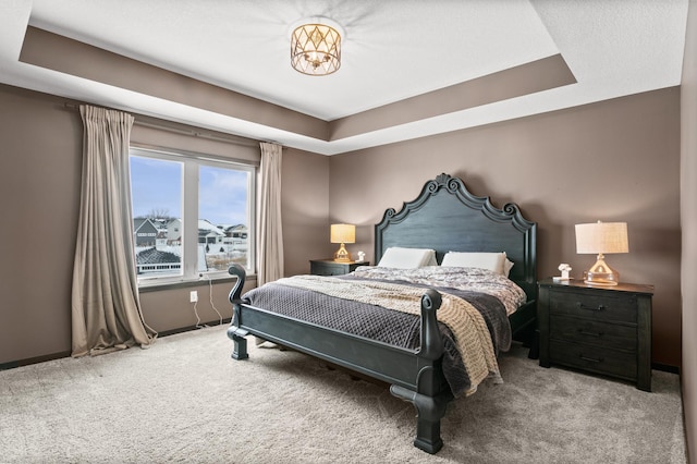 carpeted bedroom with a tray ceiling and baseboards