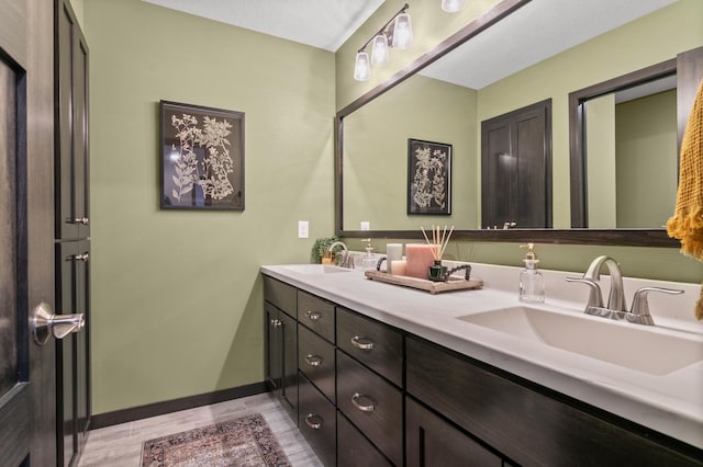 full bathroom featuring double vanity, wood finished floors, baseboards, and a sink