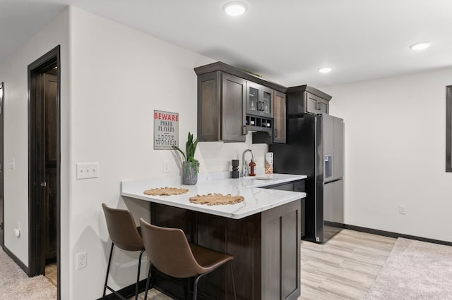 kitchen with a breakfast bar, recessed lighting, a peninsula, stainless steel refrigerator with ice dispenser, and a sink