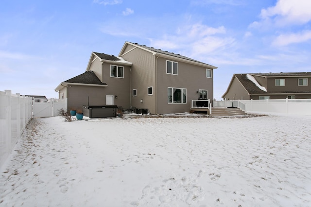 snow covered back of property featuring a gate, cooling unit, a fenced backyard, a hot tub, and a deck