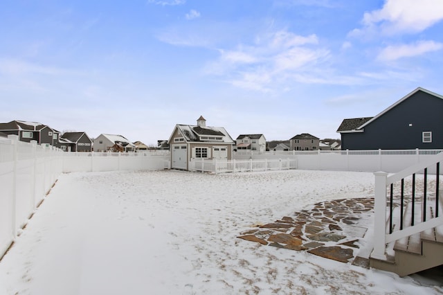 yard covered in snow featuring an outdoor structure, a fenced backyard, and a residential view