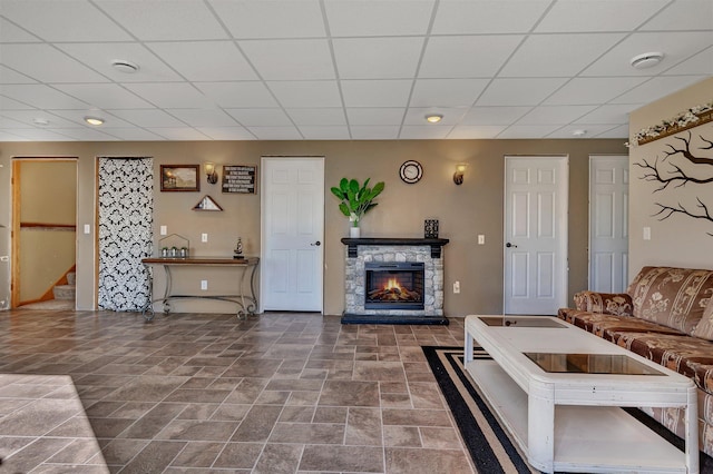 living area featuring stairs, stone finish flooring, a fireplace, and a paneled ceiling