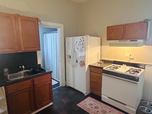 kitchen with under cabinet range hood, a sink, dark countertops, white appliances, and dark floors