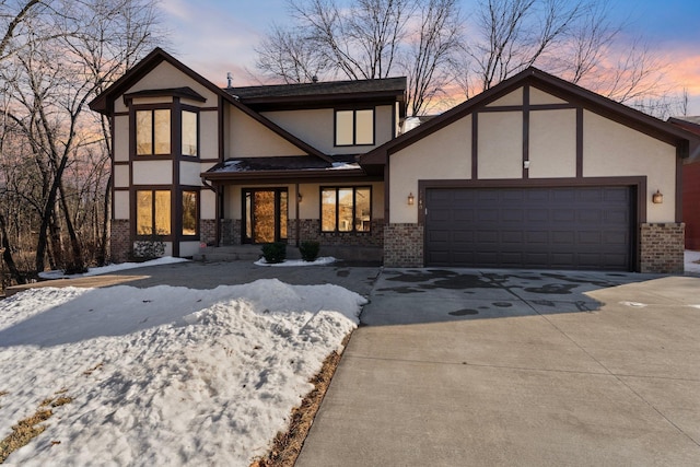 tudor-style house featuring brick siding, stucco siding, an attached garage, and driveway