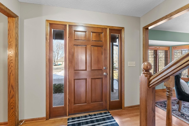 foyer featuring light wood-type flooring, baseboards, a textured ceiling, and stairs