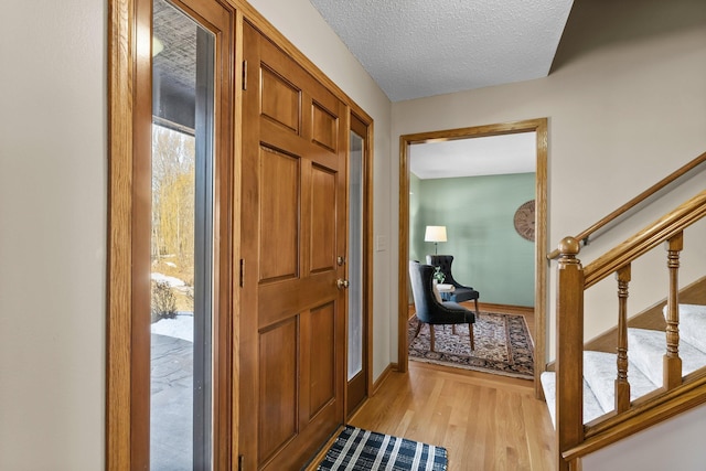 entryway with a textured ceiling, stairs, light wood-type flooring, and baseboards