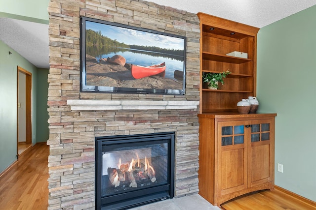 interior details featuring a fireplace, a textured ceiling, baseboards, and wood finished floors