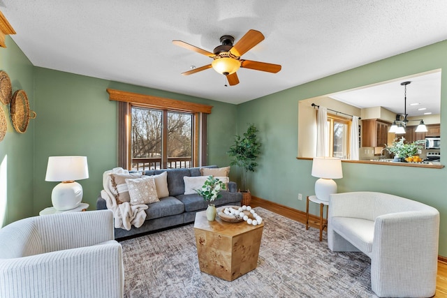 living area featuring a ceiling fan, wood finished floors, a healthy amount of sunlight, and baseboards