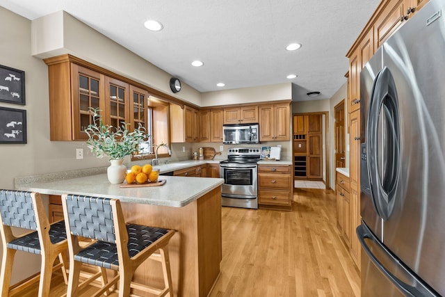 kitchen featuring a breakfast bar area, light wood-type flooring, brown cabinets, appliances with stainless steel finishes, and a peninsula