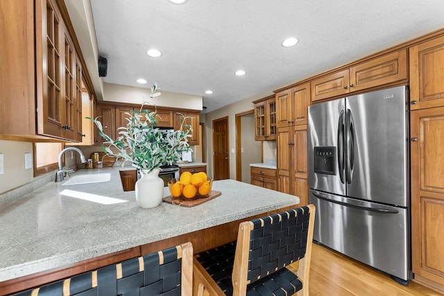 kitchen with glass insert cabinets, a peninsula, brown cabinetry, stainless steel fridge, and a sink