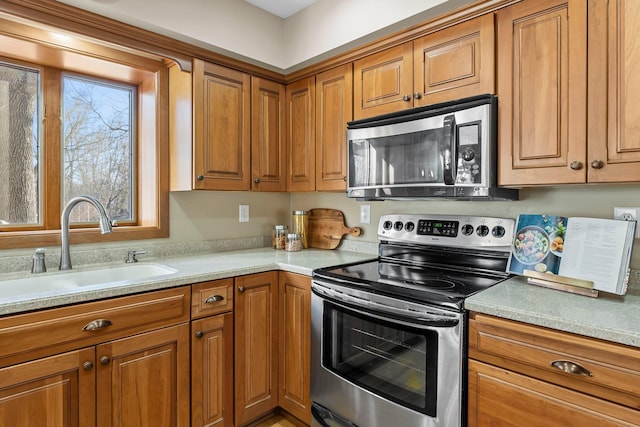 kitchen featuring a sink, stainless steel appliances, brown cabinetry, and light countertops