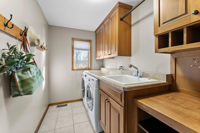 washroom with a sink, washing machine and dryer, cabinet space, light tile patterned floors, and baseboards