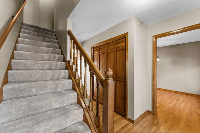 staircase with a textured ceiling, baseboards, and wood finished floors