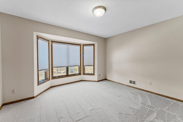 spare room featuring visible vents, a textured ceiling, carpet, and baseboards