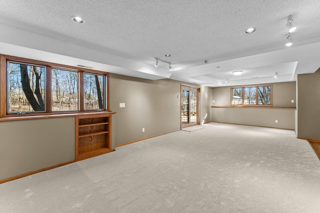 below grade area with rail lighting, baseboards, carpet floors, and a textured ceiling