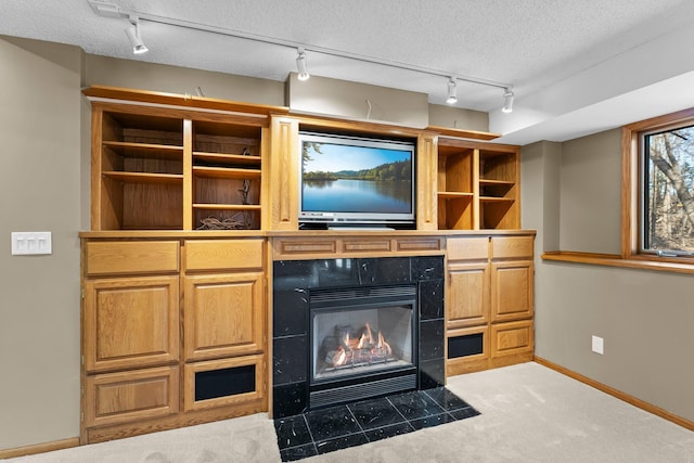 unfurnished living room with baseboards, carpet, rail lighting, a glass covered fireplace, and a textured ceiling