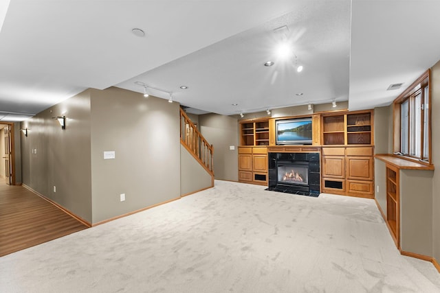 unfurnished living room featuring stairway, a fireplace with flush hearth, carpet floors, and visible vents