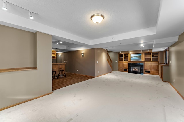 unfurnished living room with a tray ceiling, carpet flooring, and a textured ceiling