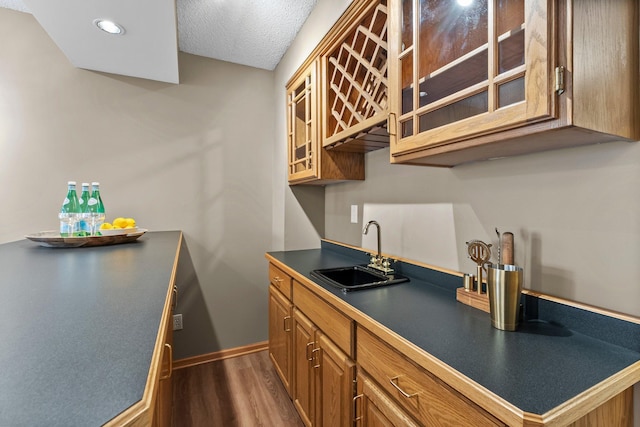 kitchen featuring a sink, glass insert cabinets, dark wood-style floors, and brown cabinetry