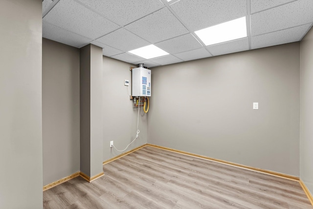 finished below grade area with a drop ceiling, light wood-type flooring, baseboards, and water heater