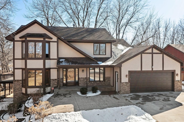 english style home featuring stucco siding, driveway, brick siding, and an attached garage